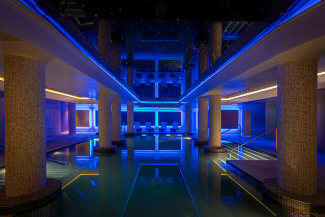 Luxurious indoor pool with columns and ambient blue lighting.